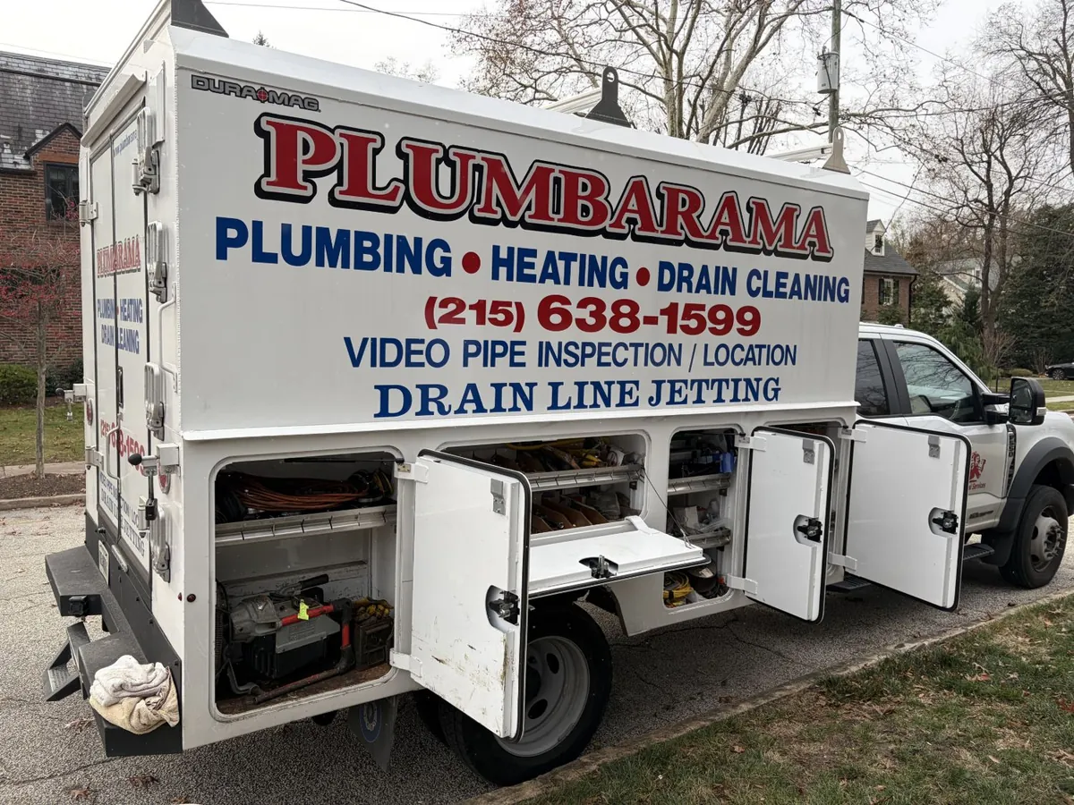 Plumbarama service truck with its side compartments open, showing a drain cleaning machine, fittings and parts