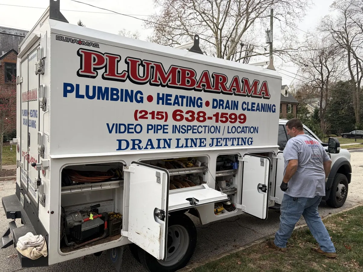 Plumbarama plumber walking to the open compartments of a stocked service truck parked on a residential street